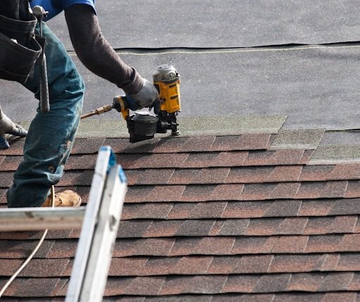 "Roofer using a nail gun to install asphalt shingles on a residential roof."